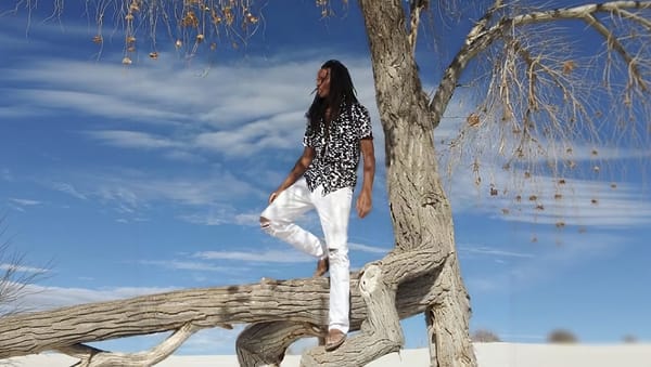 Aaron Aldana standing on a fallen tree branch under a blue desert sky