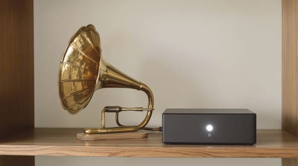 A brass gramophone horn wired to a small black home server on a shelf
