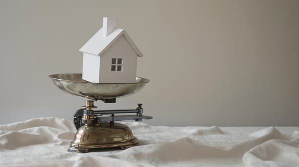 A small white model house sitting on a brass kitchen scale